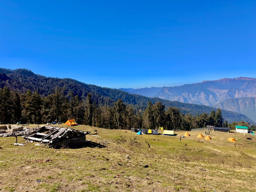 Scenic view of colorful tents in a mountain meadow under bright blue sky.